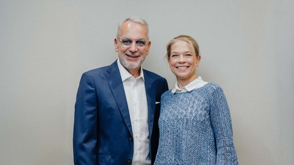 Ein älterer Mann im blauen Anzug und eine Frau im blauen Pullover lächeln freundlich