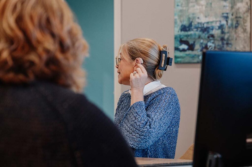 Eine blonde Frau mit Brille und blauem Pullover schaut seitlich und lächelt leicht